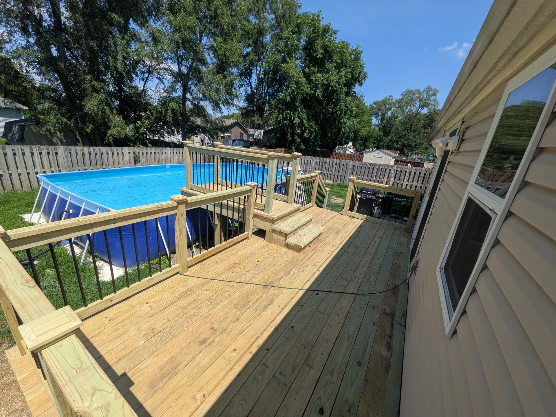 Multi-level wooden deck built around an above-ground swimming pool
